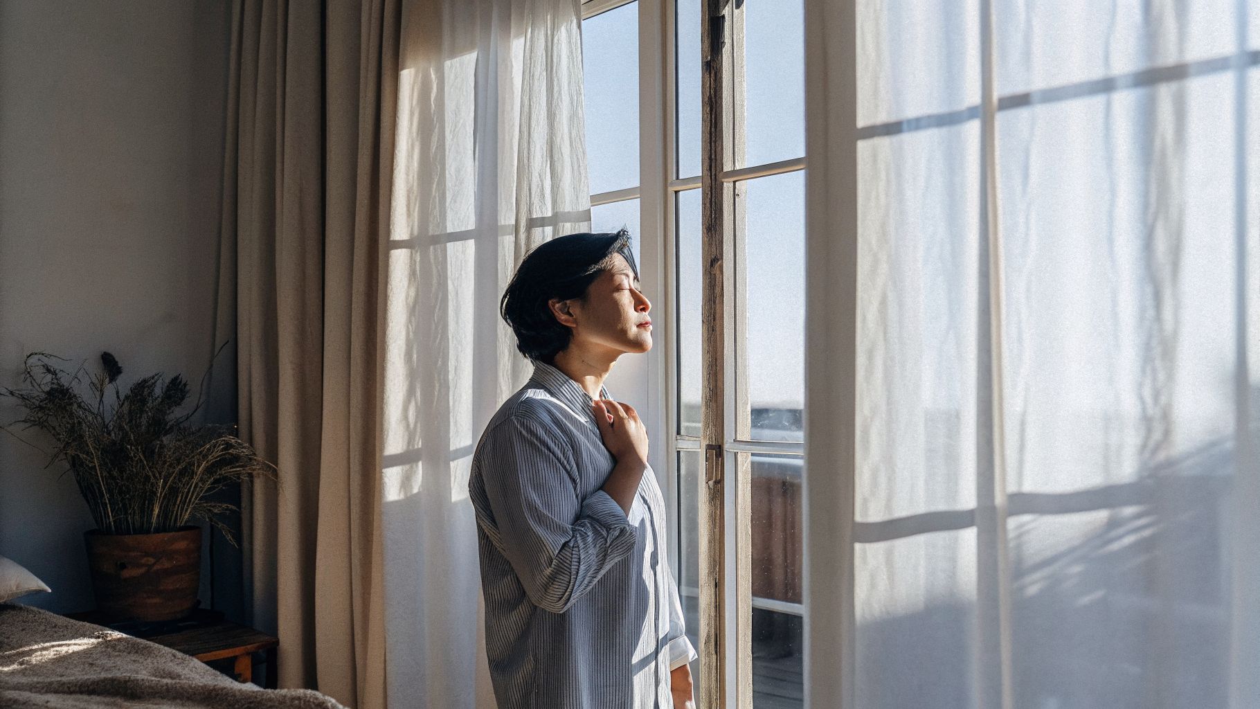 Awareness and change: a person pausing by a window with a hand on their chest