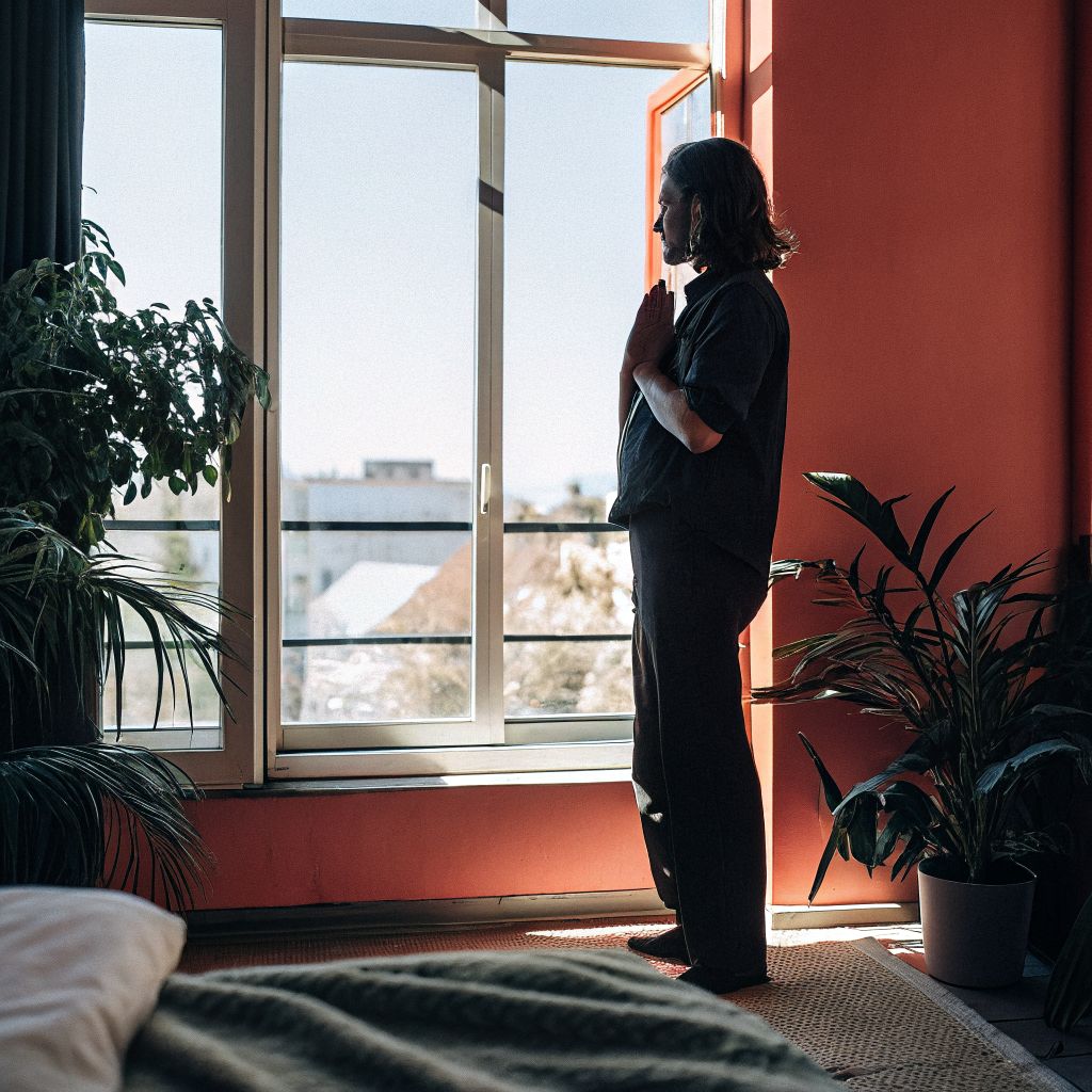 Person pausing by a window with hand on chest, practicing inner alignment before making a choice