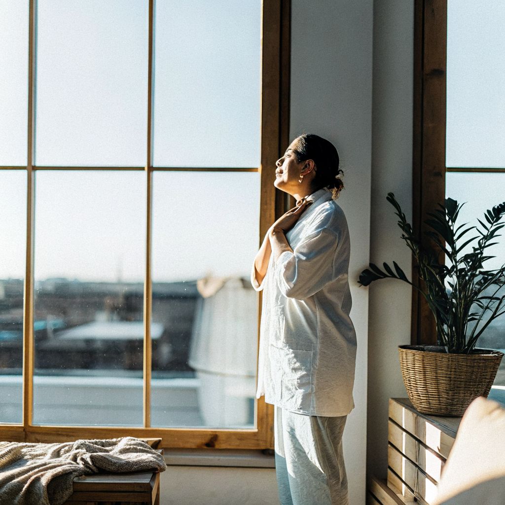Person pausing with hand on heart by a window, illustrating the space between stimulus and response