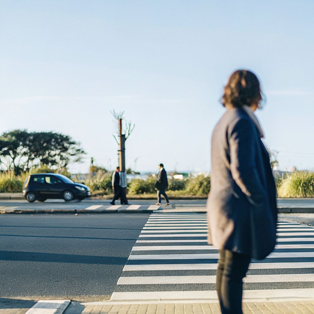 A person pausing before crossing a busy city street, illustrating the space between stimulus and response
