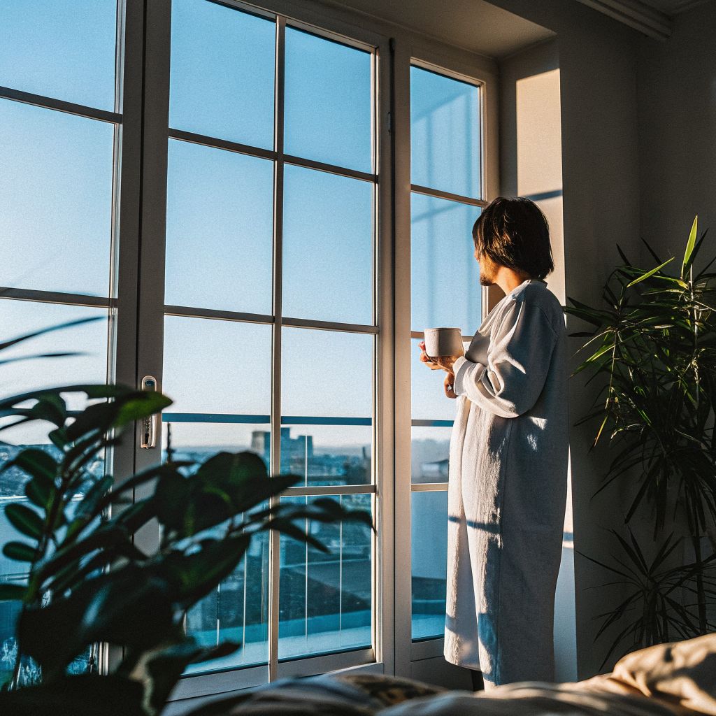 person pausing at window overlooking city