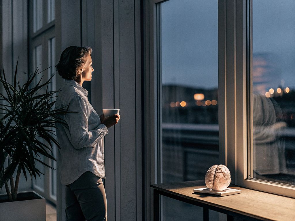 person pausing at a window with city lights, finding calm amid busyness