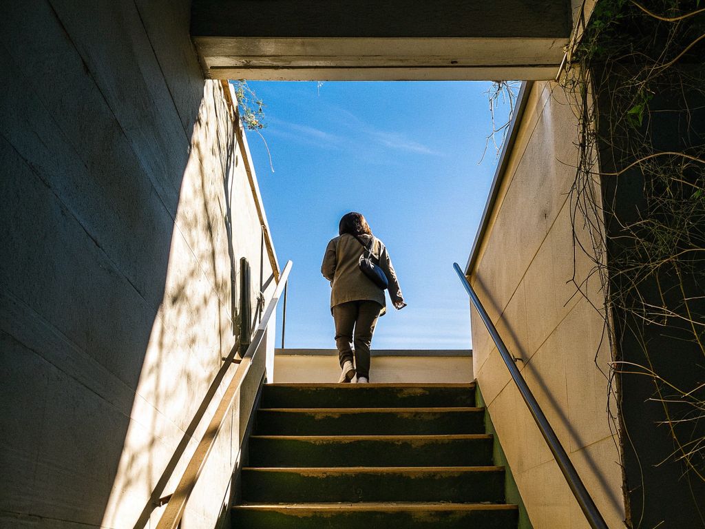 person climbing stairwell, moving from darkness into light