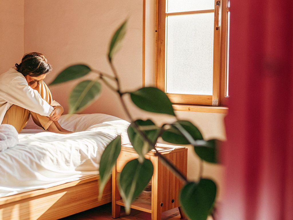 A person sitting reflectively on the edge of a bed
