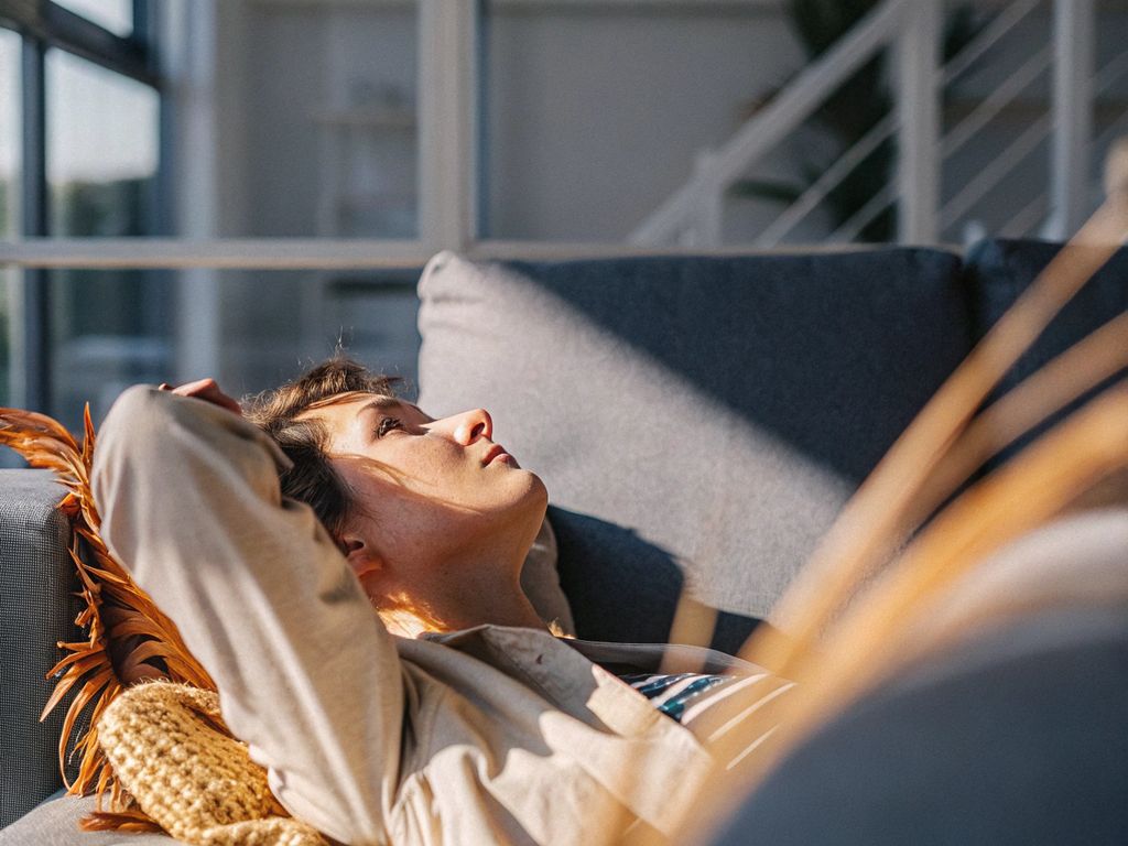Person lying on couch in natural light, looking thoughtful