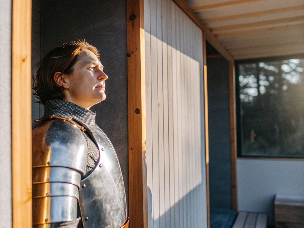 a person pausing in reflection, light shining through a small opening in heavy armor
