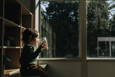 Child holding glitter jar near classroom window