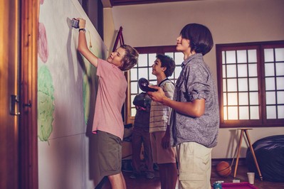 Teens painting a climate mural beside portable air sensors in an open gym
