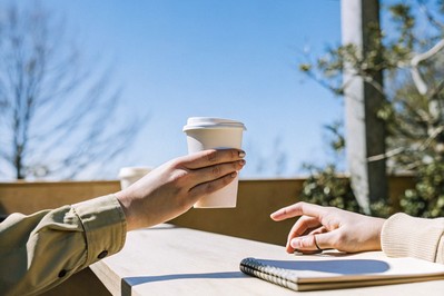 hands passing a paper cup across a counter in morning light