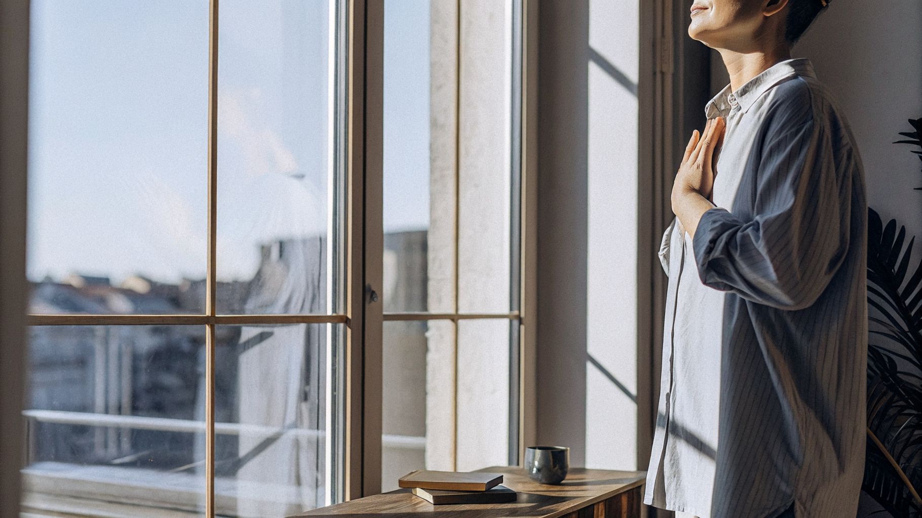 Awareness and change begins with a small pause—person by a window with hand on heart
