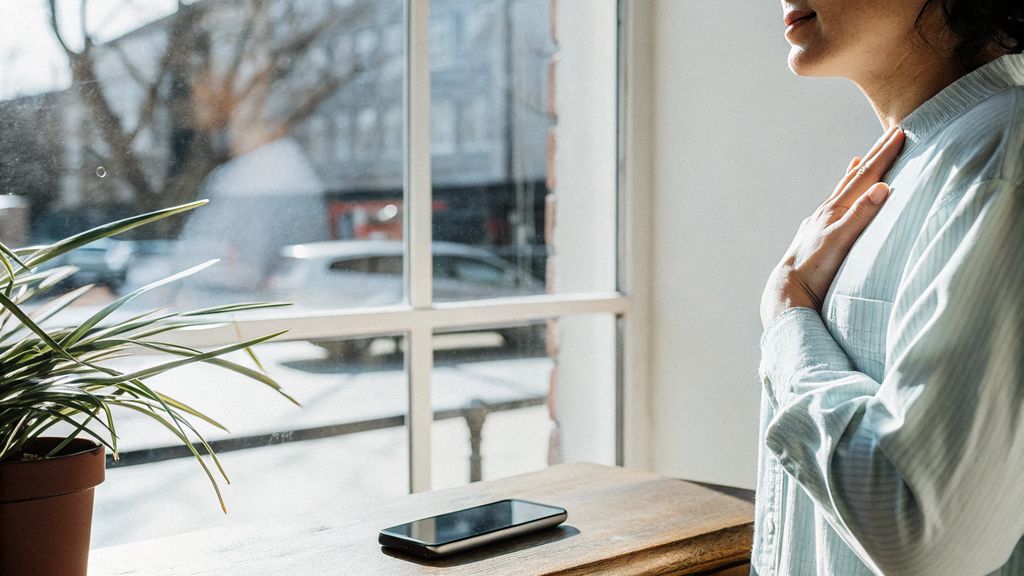 Person pausing by a window, practicing mindful awareness before reacting