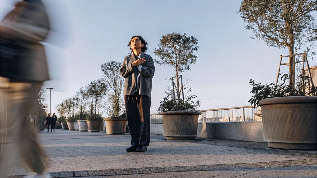 Person pausing in a busy city, hand on chest, taking a breath